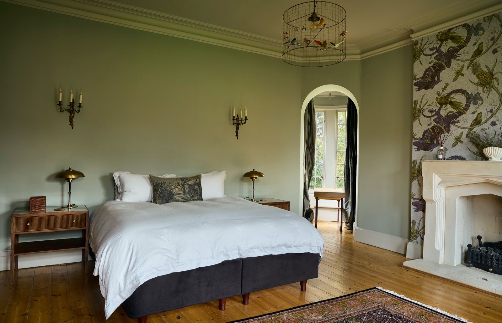 A pale green bedroom with a fireplace and an arched doorway