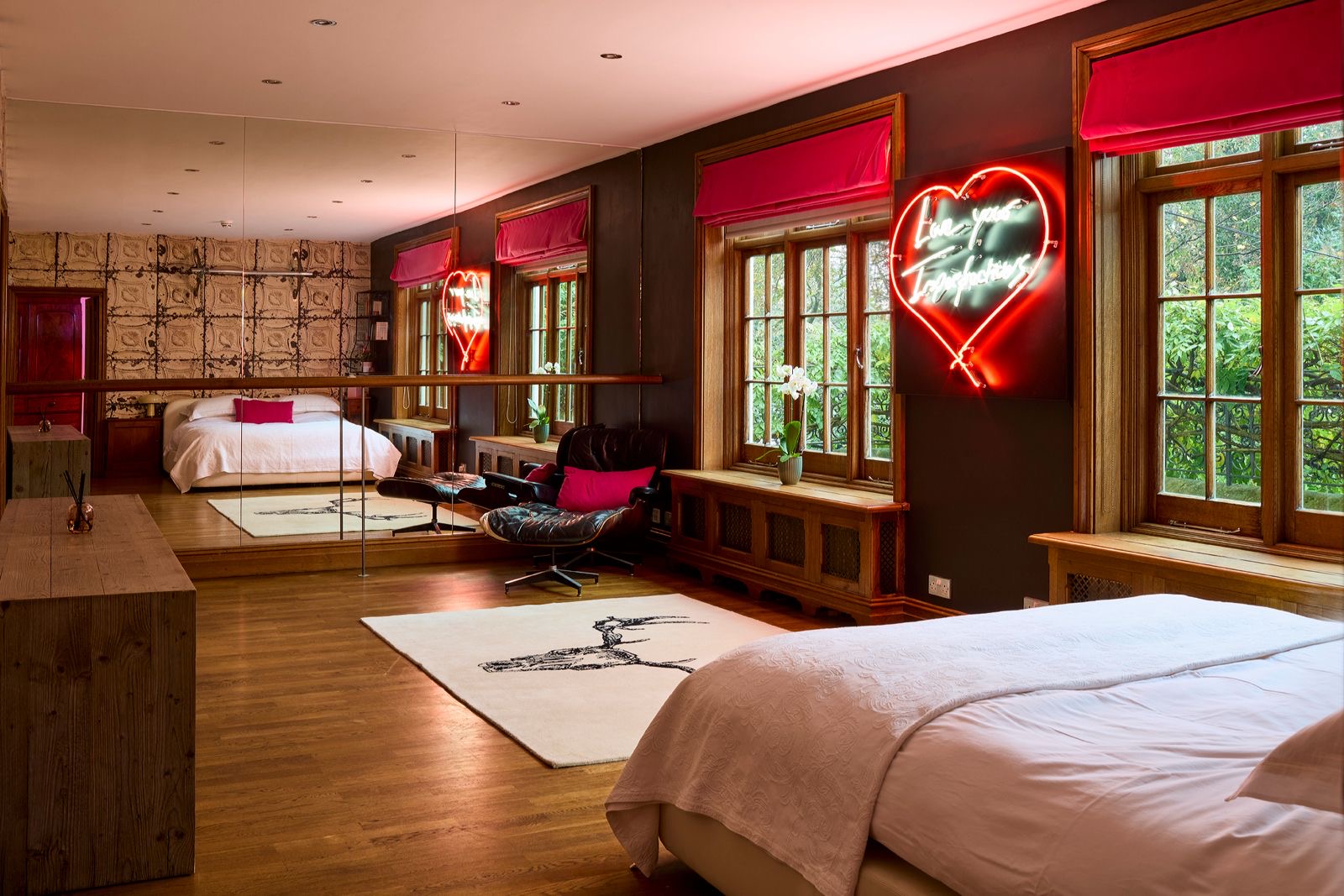 A bedroom with a neon heart and windows onto the garden
