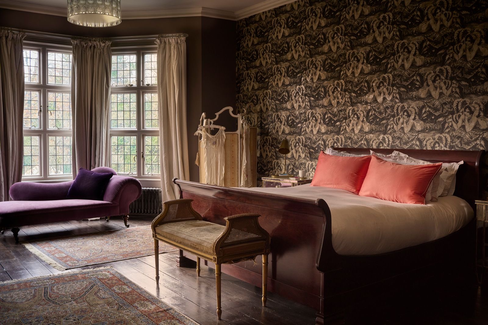 A bedroom with toile wallpaper and coral cushions