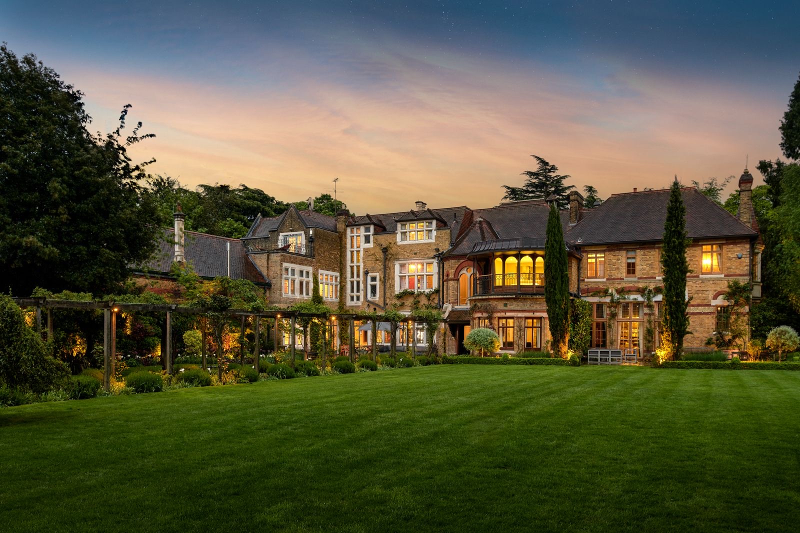 The back of the home lit up at dusk above a wide lawn
